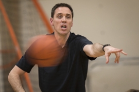 Men’s basketball coach Landry Kosmalski with a basketball in front of him he named NCAA Division III National Coach of the Year.